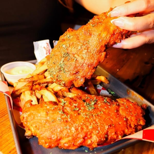 A hand holding up a piece of SideChick HTX fried chicken over a tray of fries and sauce.