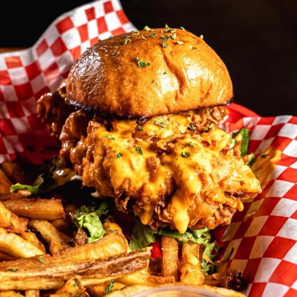 A SideChick HTX fried chicken sandwich with cheese sauce, lettuce, and fries in a red checkered basket.