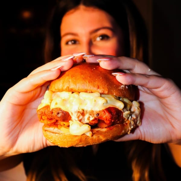 A person holding a SideChick HTX fried chicken sandwich topped with mac and cheese.